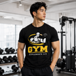 Muscular male fitness model standing in a gym wearing a black Gym T-Shirt featuring the yellow Gym Supplements U.S graphic logo.