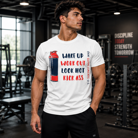 Muscular male fitness model standing in a gym wearing a white Gym Supplements U.S Kick Ass T-Shirt, featuring a red and blue shaker bottle graphic alongside the text "WAKE UP, WORK OUT, LOOK HOT, KICK ASS".